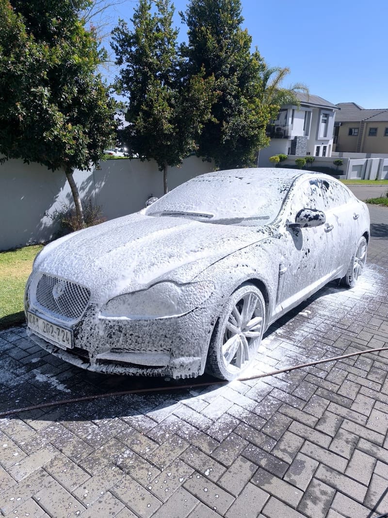 The same Jaguar XF covered in a full blanket of snow foam during the pre-wash stage