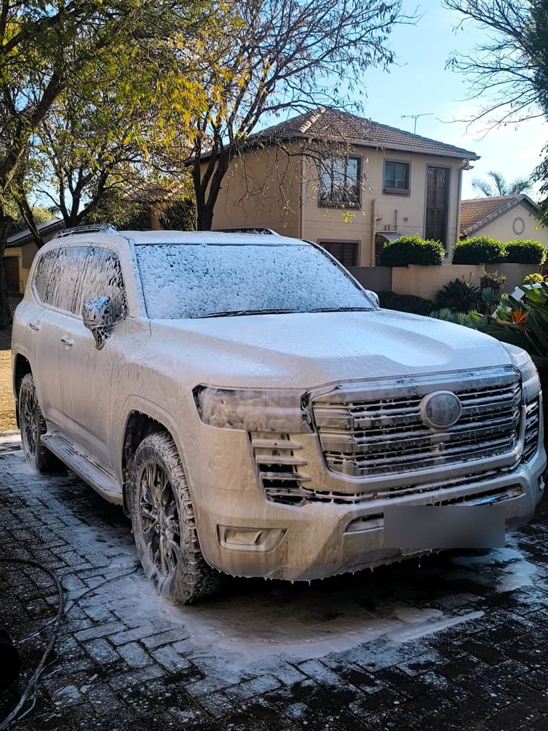 Toyota Land Cruiser 300 under a full coat of snow foam on a driveway during a mobile wash